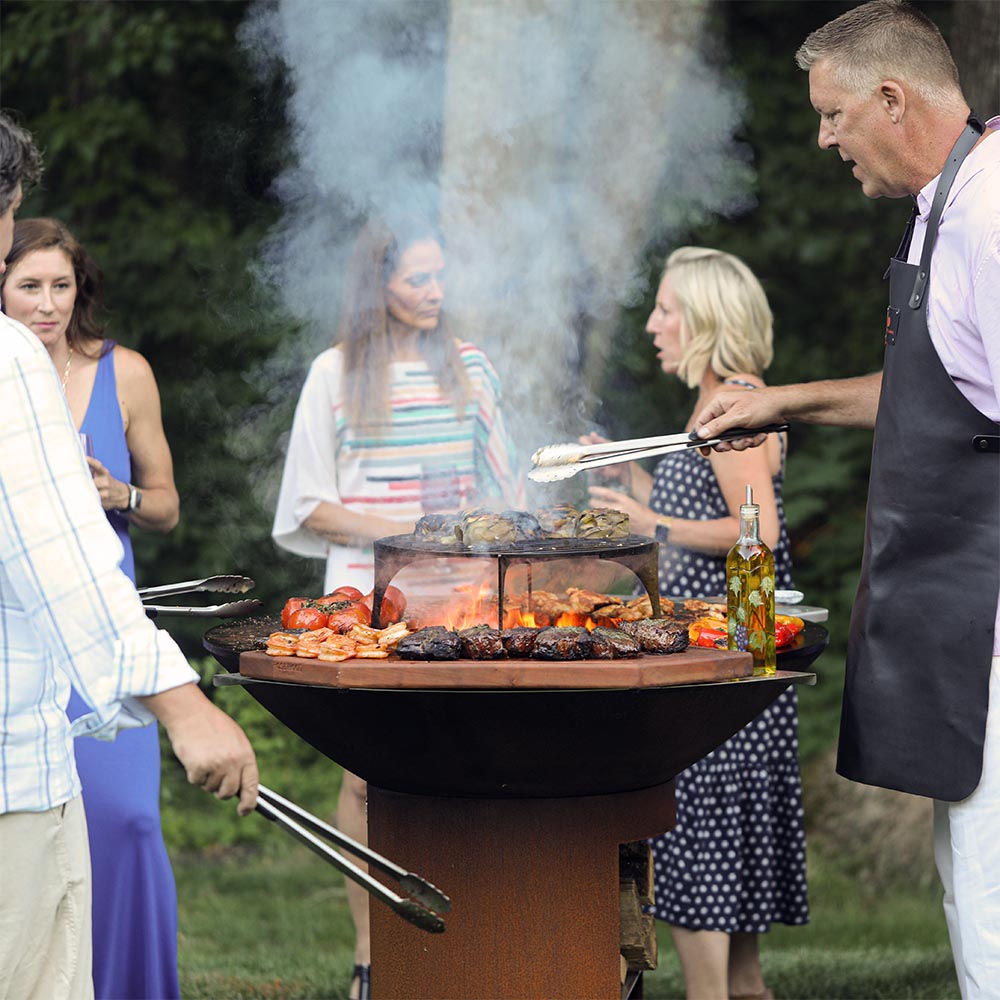 Friends grilling around a wood-fired grill in a garden